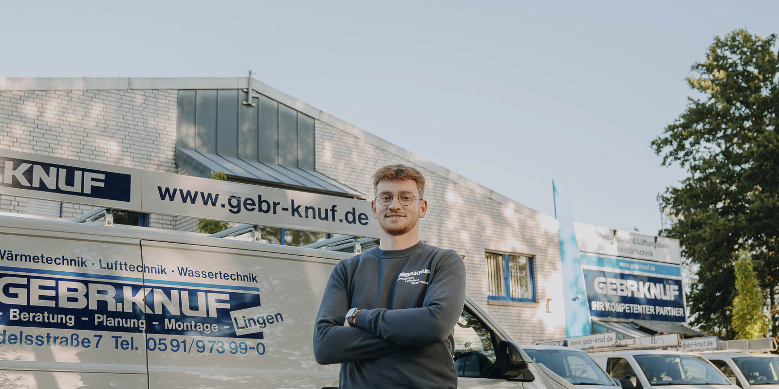 Ein junger Mann mit Brille steht selbstbewusst vor einem Firmenfahrzeug, das mit dem Logo von GEBRKNUF beschriftet ist.