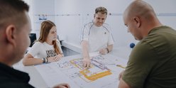 Eine Gruppe von vier Personen diskutiert über einen detaillierten Plan auf einem Tisch, während sie konzentriert schauen.