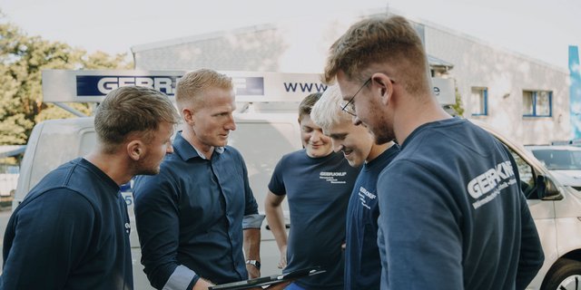 Eine Gruppe von fünf Männern, die konzentriert auf ein Tablet schauen, während sie in einem Außenbereich stehen.