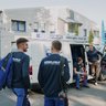 Fachleute in Arbeitskleidung vor dem Firmenfahrzeug Ein Team von Technikern bereitet sich vor, um einen Auftrag zu erledigen, während der Lieferwagen im Hintergrund parkt.