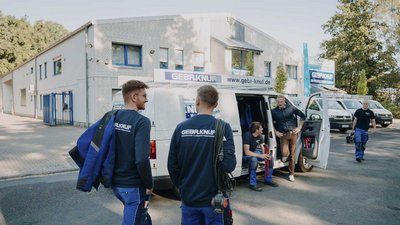 Fachleute in Arbeitskleidung vor dem Firmenfahrzeug Ein Team von Technikern bereitet sich vor, um einen Auftrag zu erledigen, während der Lieferwagen im Hintergrund parkt.