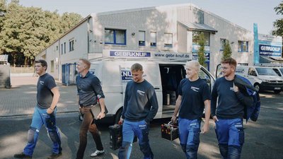Die Gruppe von Handwerkern trägt Werkzeugkisten und zeigt eine freundliche Atmosphäre vor dem Bürogebäude.