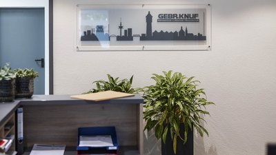 Ein moderner Empfangsbereich mit Pflanzen und einem klaren Schild, das den Firmennamen GEBR.KNUF zeigt.