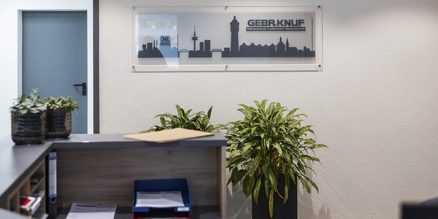 Ein moderner Empfangsbereich mit Pflanzen und einem klaren Schild, das den Firmennamen GEBR.KNUF zeigt.