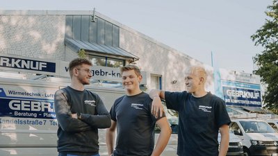 Die drei Männer unterhalten sich entspannt, während sie vor einem Fahrzeug mit dem Logo ihrer Firma stehen.