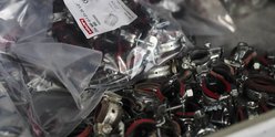 Eine Vielzahl von Metallklemmen mit roten Gummibändern liegt in einer Schachtel, einige sind in Plastiktüten verpackt.