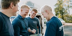 Die Gruppe von Männern diskutiert fröhlich, während sie an einem Fahrzeug stehen und Informationen austauschen.